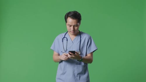 Asian Male Doctor With Stethoscope Using Smartphone While Walking On Green Screen Background