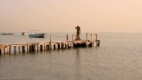 Woman relaxing with blowing on her dress, walking on wooden pier with boats floating on water over s