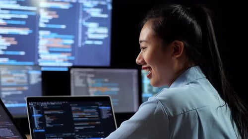 Visão traseira de uma programadora asiática olhando o banco de dados no tablet e escrevendo o código em um laptop