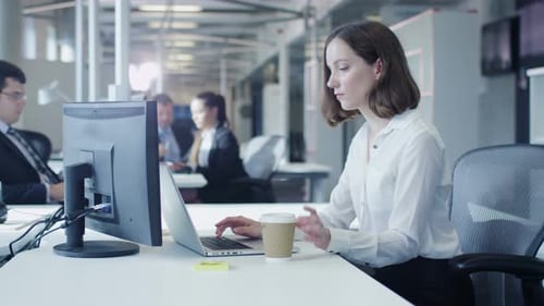 Female Office Worker is Working on Laptop and Drinking Coffee