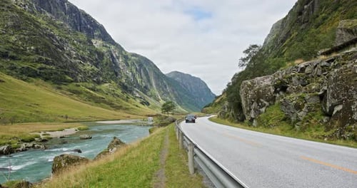 Norwegian Mountain Road Beside Turquoise Glacial River with Cars in Motion