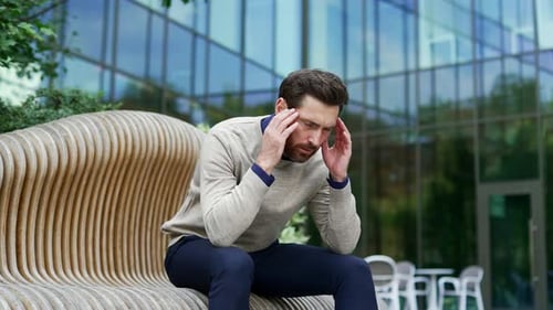 Businessman sitting on bench outside in urban environment feels stress and depression.