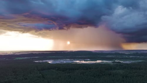 Dark storm clouds pouring rain with glowing sunshine from behind, aerial view