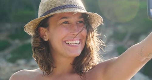 Beautiful young girl doing selfie at the sea, smiling waving at the camera, in a swimsuit in a str