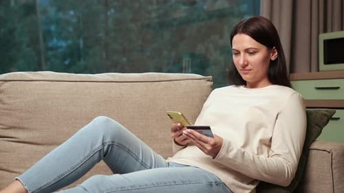 Woman Using Phone and Credit Card on Couch