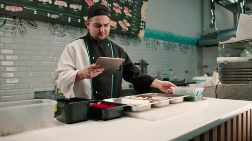 A pensive sushi chef with a tablet in his hands looks at recipes for delicious rolls and ingredients