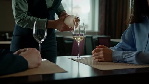 A date in a hotel restaurant a man and a woman drink white wine in glasses the waiter pours wine