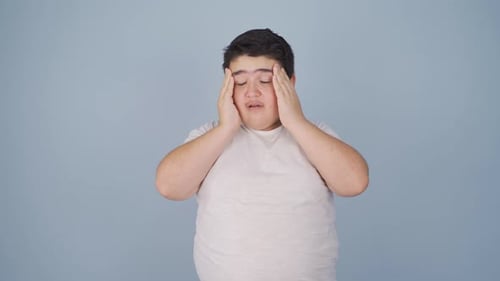 Teen Covering Eyes with Headache on Blue Background