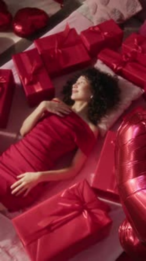 Vertical Portrait of Gen Z Woman Lying on Bed Surrounded by Gift Boxes