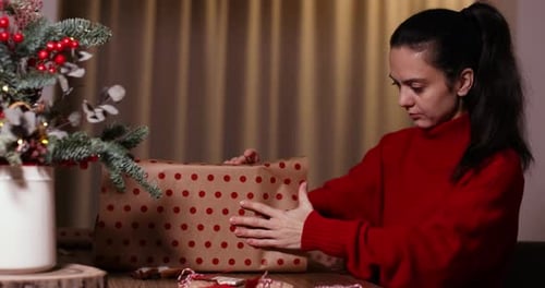 Woman wrapping Christmas gift with care at table