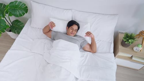 Asian handsome young man getting up from sleep on bed in the morning.
