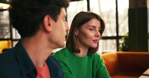 Expressive Beautiful Woman Gesturing While Talking with Man Sitting in Modern Cafe
