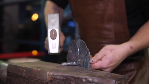 Worker in Apron Pats Metal Flower with Hammer at Workbench