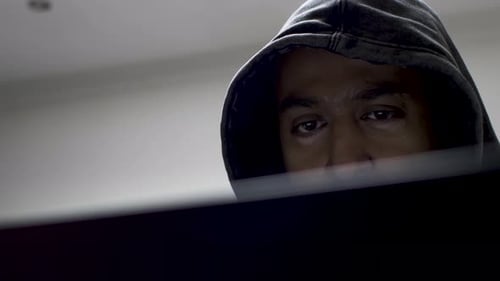 A close up shot of an unidentified underground hacker wearing a hoodie, the man's eyes fixed on the