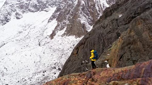 Mountaineer Walking on Snow with Trekking Poles Near Snowy Mountain Range