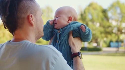 Young Father Holds His Newborn Baby Son in His Arms in a Park