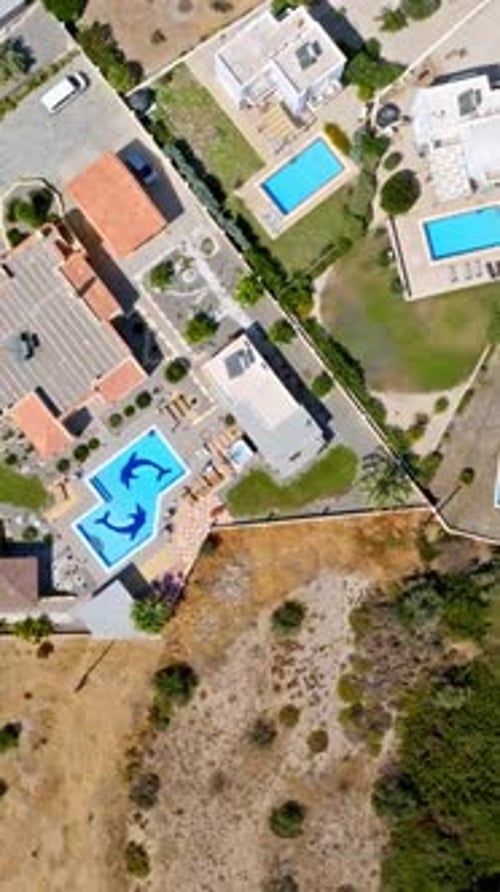 Vertical drone shot rotating above vacation homes with pools in sunny Greece