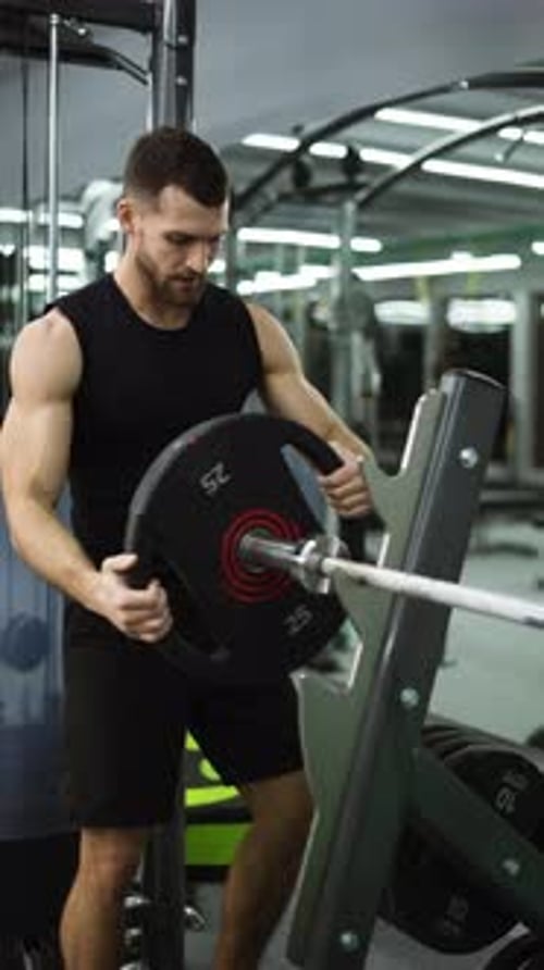 Male Athlete Preparing for Intensive Workout Loading Heavy Plates on Barbell