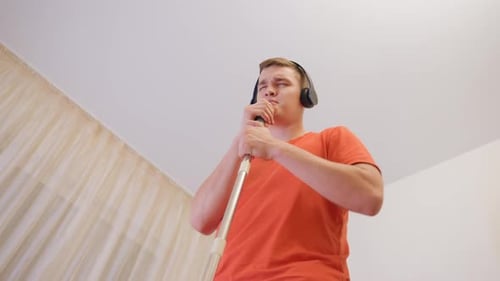 Vista hacia arriba del hombre cantando en el mango de la mopa con auriculares
