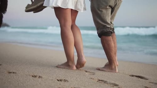 Slow motion handheld shot of a couple in love walking along the sand on the beach in front of the se