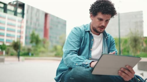 Close-up, man sitting and using tablet outdoors on modern buildings background
