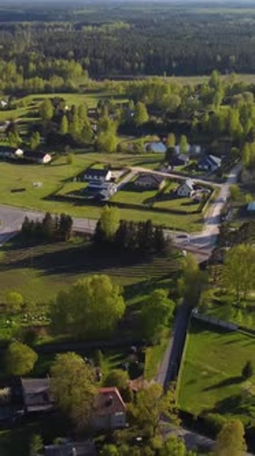 Vertical slow drone pull away over Katlakalns residential area, spring fields, traffic, and houses