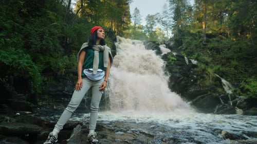 Schöne Touristin, die im Wald spaziert, Porträt einer Reisenden vor einem Wasserfall