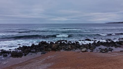Waves crash on rocky shore near the ocean under cloudy sky
