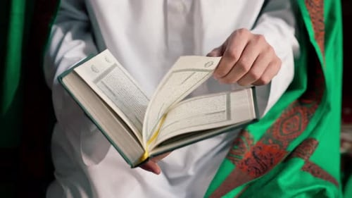 Close-up of the hands of a Muslim who sitting on his knees prays with Holy Quran in the mosque