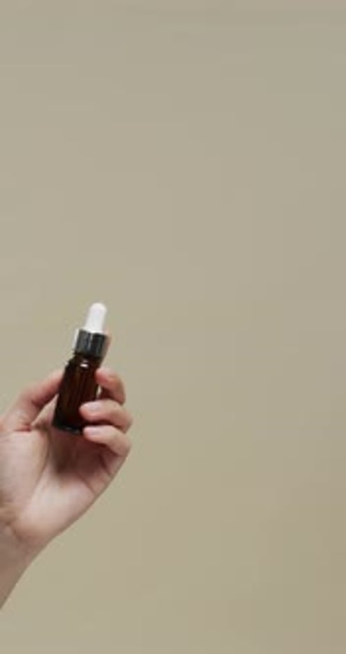 Vertical video of hand of woman holding cosmetic on beige background with copy space, slow motion