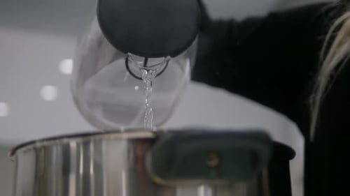 Slow motion pouring boiling water from a kettle into a pot.