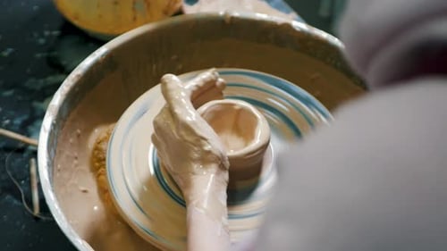 Close-up of potter's hands covered with clay making beautiful vase on throwing wheel in pottery work