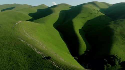 A Lone Car Navigates Through the Rugged Terrain of a Lush Green Hill Surrounded By Meadows and