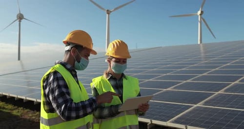 Arbeiter mit Schutzmasken überprüfen das Projekt für erneuerbare Energien auf einem digitalen Tablet