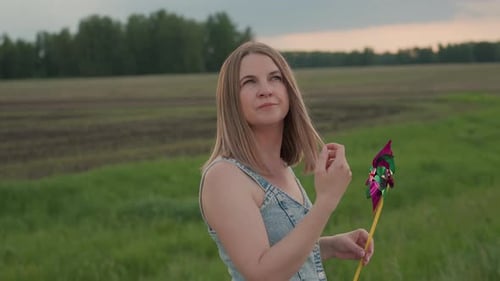 Lady Adjusting Hair with Pinwheel in Grassy Field Breeze