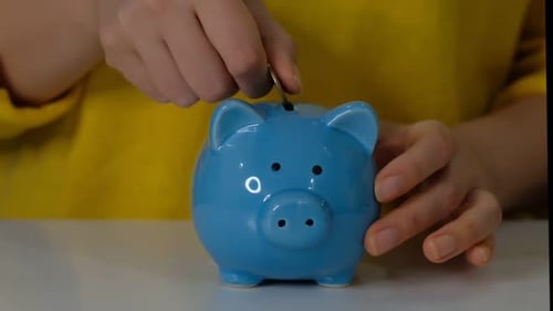 Piggy Bank Business Concept A Hand is Putting a Coin in a Piggy Bank on a Blue Background Saving