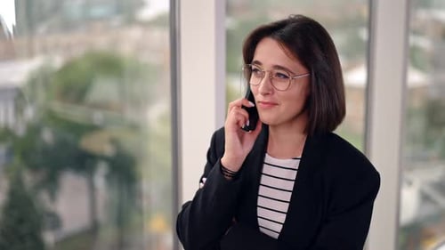 Beautiful positive lady stands at the window speaking on the phone.