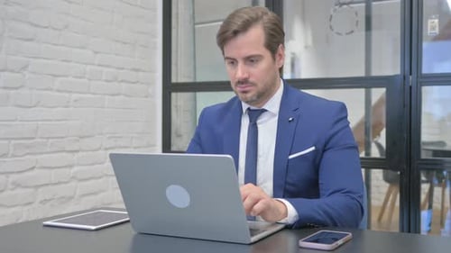 Man in Suit Types on Laptop at Desk