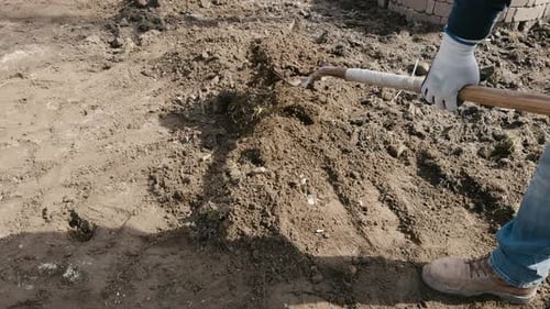 Person Spreading Dirt with Shovel on Bright Day