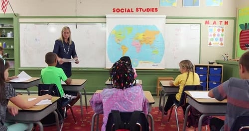Teacher smiling distributing papers to diverse elementary school class