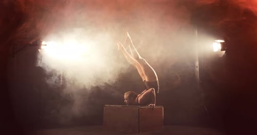 Una mujer contorsionista en una dramática escena llena de humo hace que el pecho se ponga de pie sobre una caja