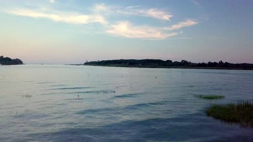 aerial drone shot of lagoon with backlight and flare during sunset with birds
