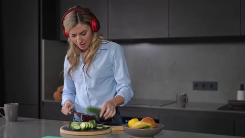 Woman in Kitchen Chopping Cucumber While Listening to Music