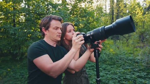 Birdwatching in park. Couple watch birds with binoculars and camera with telephoto lens. Amateur bir