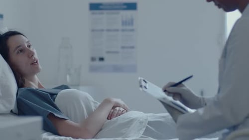 Female Doctor Speaking with Sick Woman and Making Notes in Hospital Ward