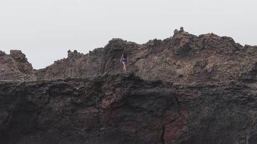 Young Female Hiker Traversing Volcanic Crater Rim Gazing Across Rugged Landscape with Expansive