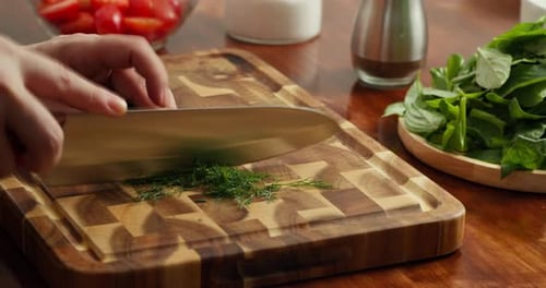 Nahaufnahme eines Küchenchefs, der frische Frühlingszwiebeln, Petersilie und Dill auf einem Holzschneidebrett hackt