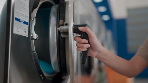 Close up shot of a woman hands as she interacts with a commercial washing machine. The image speaks