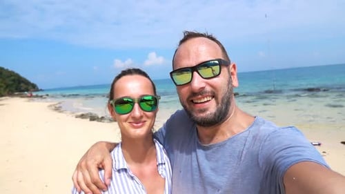 Happy young couple embracing taking selfies on tropical beach in slow motion