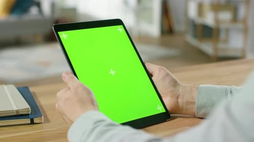 Man Using Hand Gestures on Green Mock-up Screen Digital Tablet Computer in Portrait Mode while Sitt